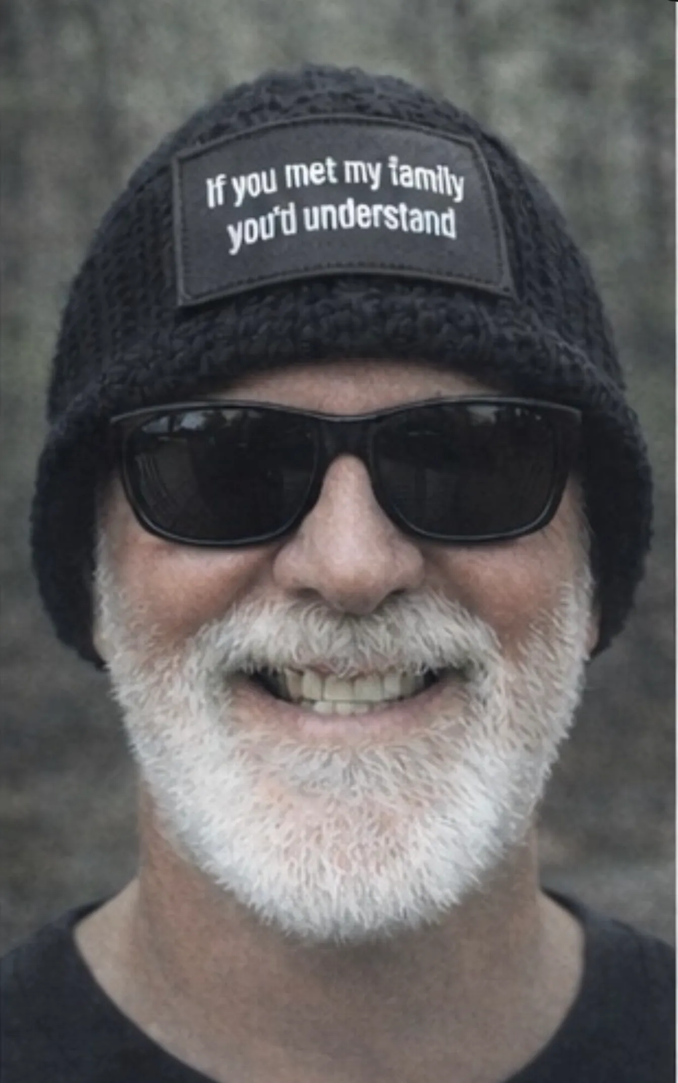 An adult man wearing a black ribbed beanie with a text patch.