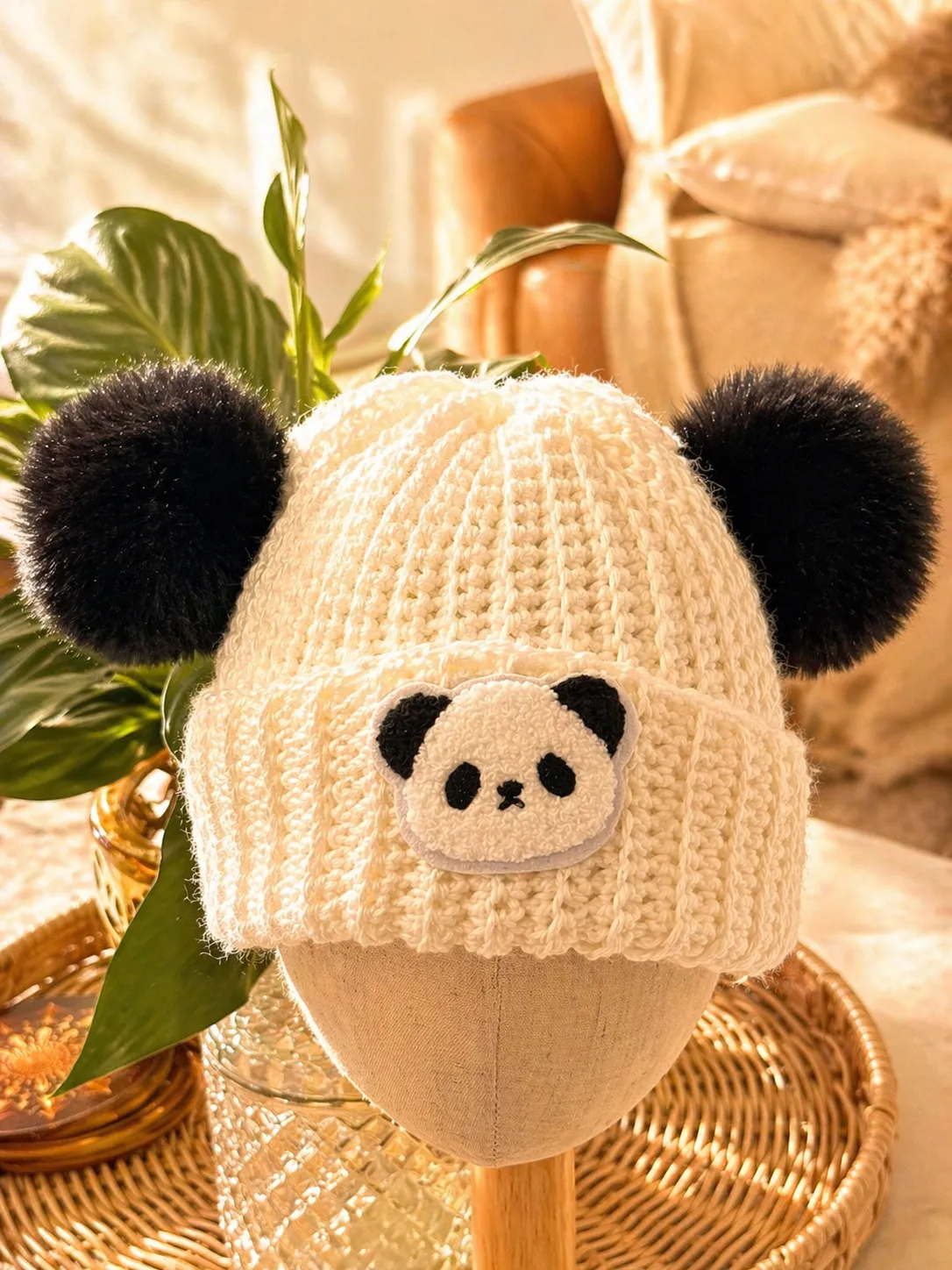 Hand-crocheted cream beanie with an embroidered panda face and two black fuzzy pom poms positioned ears