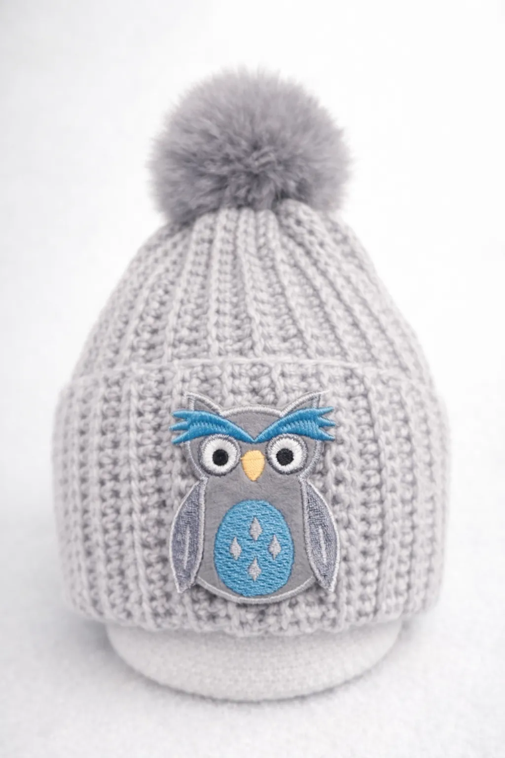 Dove-grey ribbed kids beanie with smoky pom and a blue-and-grey crocheted owl.